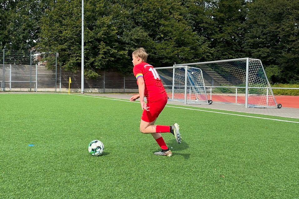 Fu&szlig;ballspieler in rotem Trikot sprintet &uuml;ber ein Kunstrasenfeld in Richtung Ball. Im Hintergrund stehen Tore.