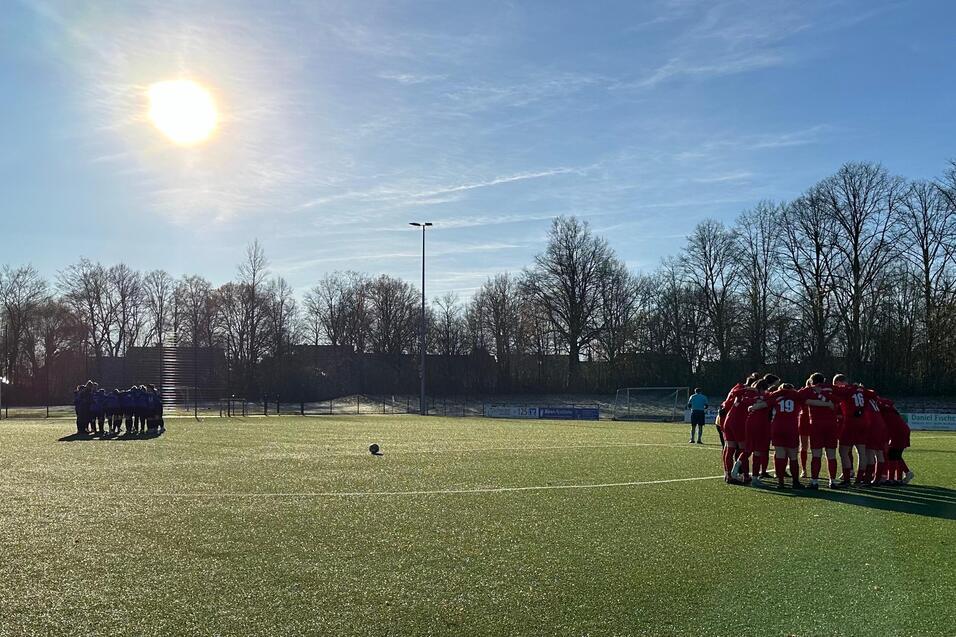 Zwei Fu&szlig;ballmannschaften in ihren Trikots stehen sich auf einem Rasenplatz gegen&uuml;ber, Sonnenlicht am Himmel.
