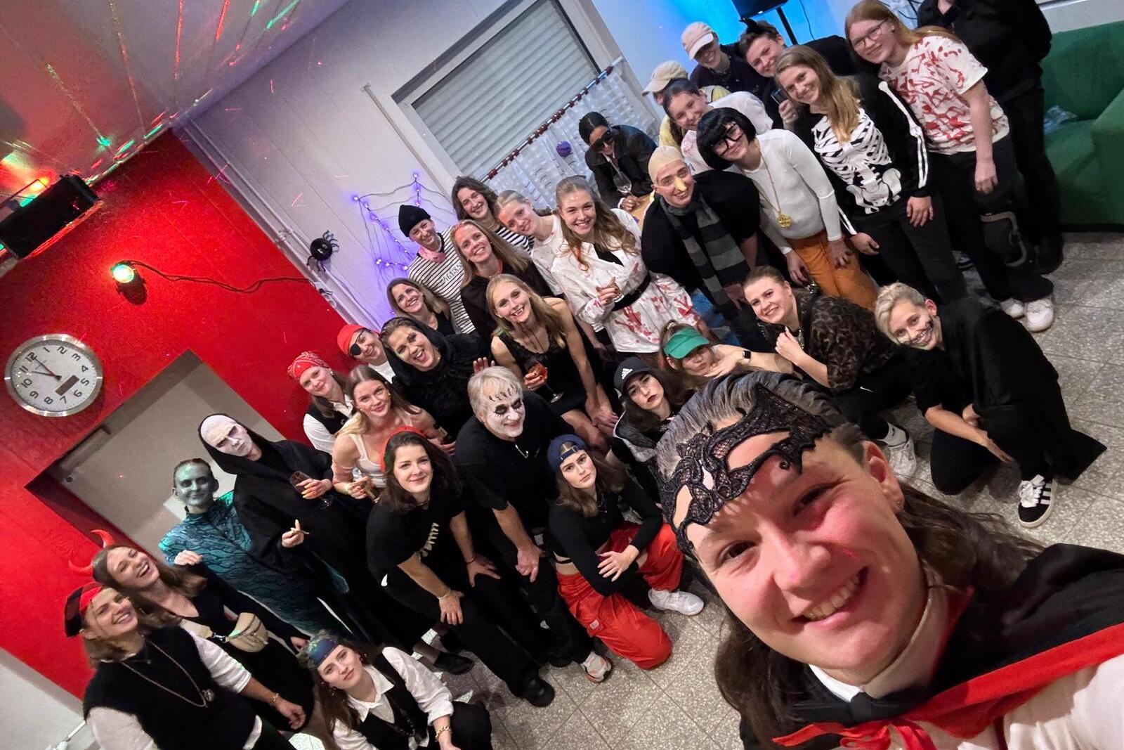 Gruppenselfie auf einer Mottoparty mit verkleideten G&auml;sten, die in bunten Kost&uuml;men und Masken posieren.