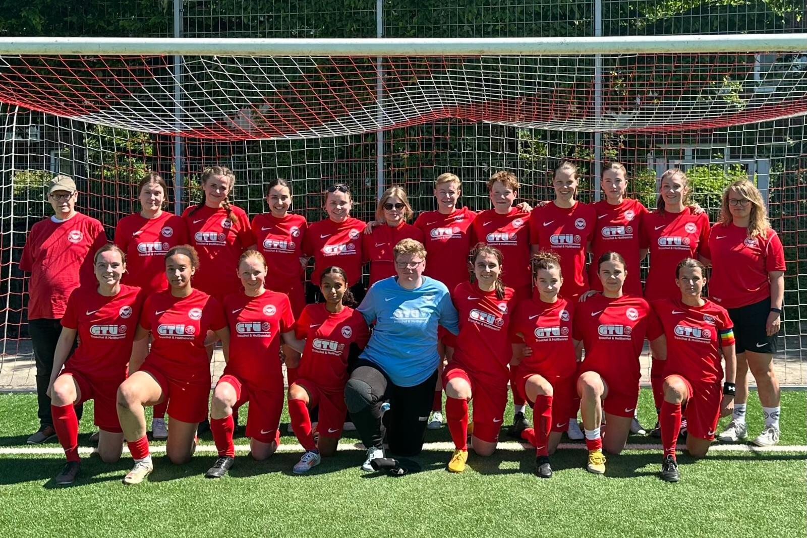Mannschaftsfoto einer Frauenfu&szlig;ballmannschaft in roten Trikots vor einem Tor auf einem Fu&szlig;ballplatz.