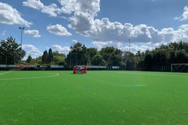 Gruppierung von Spielern auf einem Kunstrasenfeld unter blauem Himmel mit Wolken.