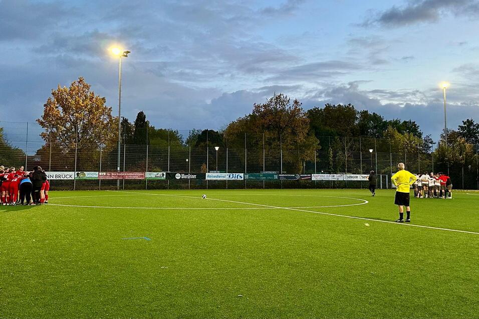 Fu&szlig;ballmannschaft in roten Trikots versammelt sich auf dem Kunstrasenfeld, w&auml;hrend der Schiedsrichter zusieht.