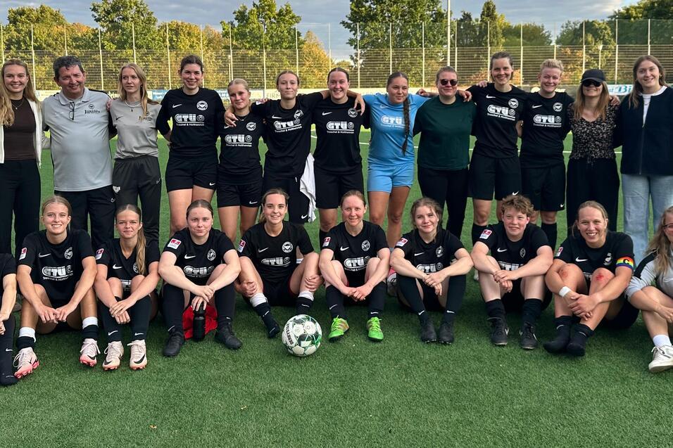 Mannschaftsfoto einer Fu&szlig;ballmannschaft mit Trainer und Spielern, die auf einem Kunstrasenfeld posieren.