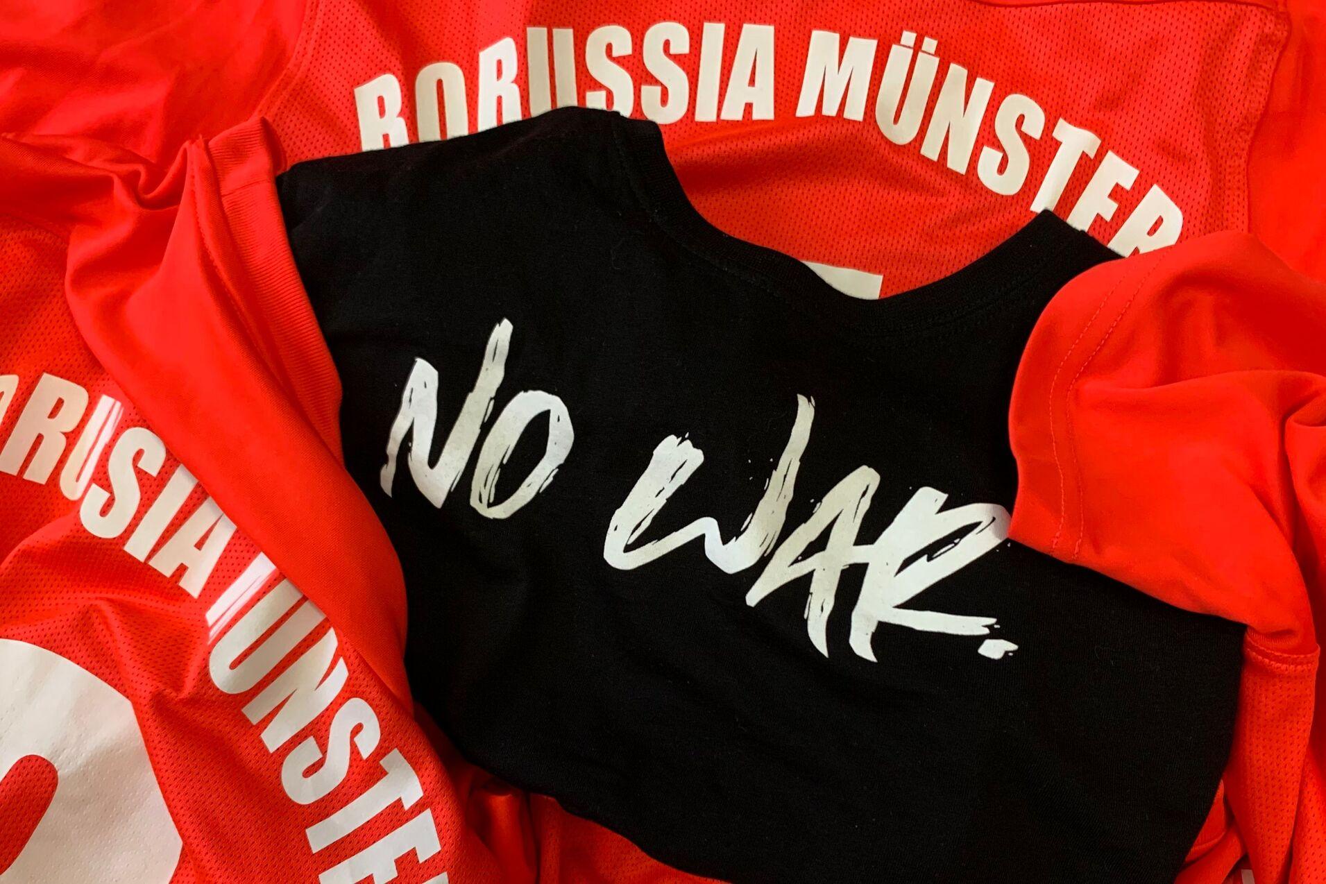 Rote Trikots mit der Aufschrift &bdquo;Borussia M&uuml;nster&ldquo; und einem schwarzen Shirt mit der Aufschrift &bdquo;NO WAR.&ldquo; in der Mitte.