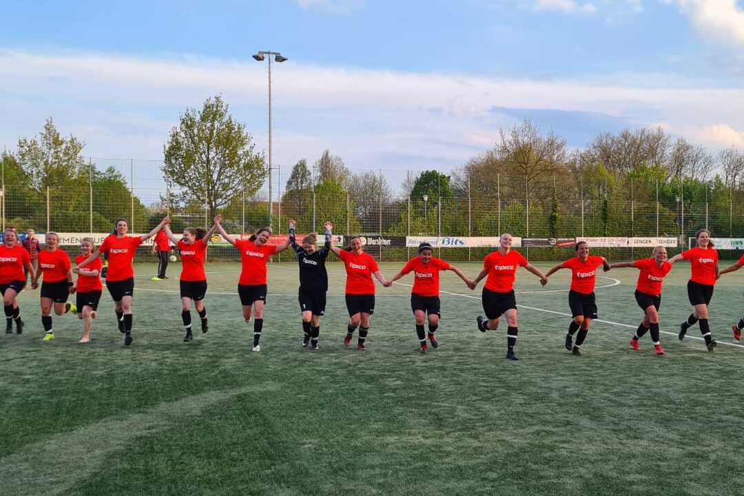 Eine Gruppe von Fu&szlig;ballspielerinnen in roten Trikots l&auml;uft Hand in Hand auf einem Kunstrasenfeld.