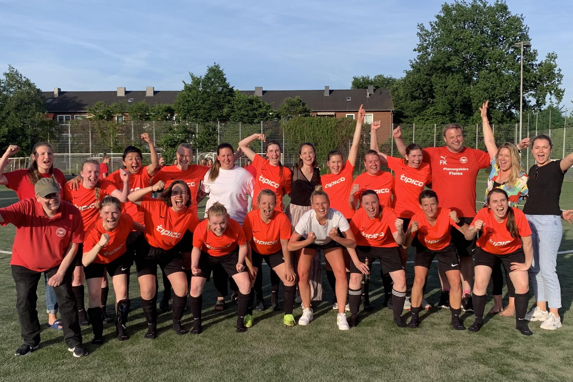 Gruppe von Frauen im roten Trikot jubelt auf einem Fu&szlig;ballplatz, einige halten Flaschen in der Hand.