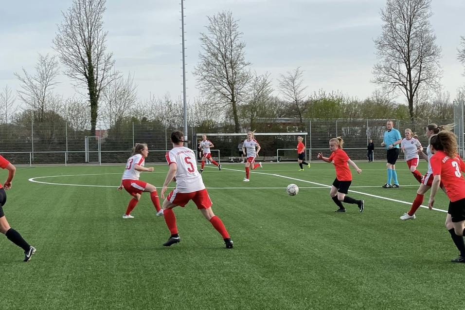 Fu&szlig;ballspiel zwischen zwei Teams auf einem Kunstrasenplatz; Spielerinnen in roten und wei&szlig;en Trikots laufen dem Ball nach.
