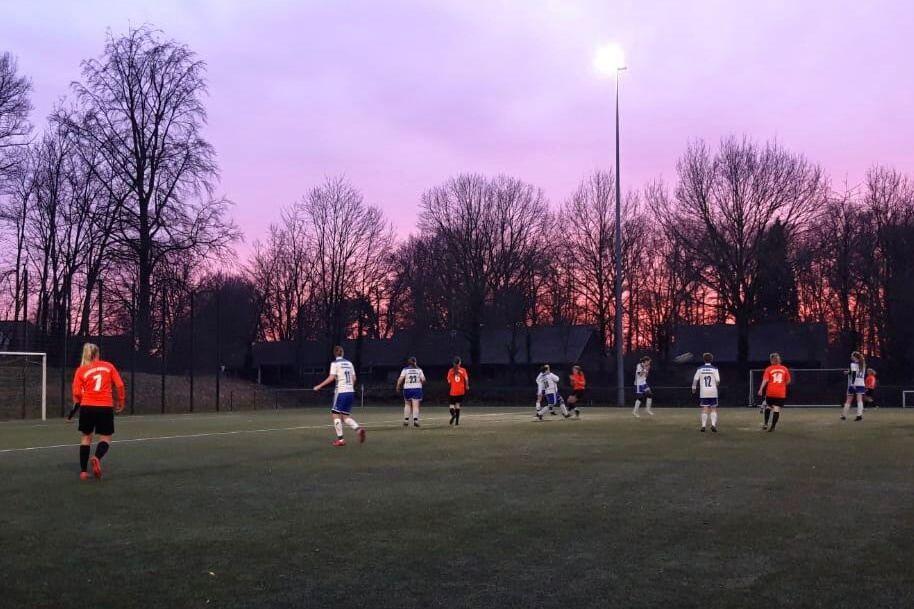 Fu&szlig;ballspiel auf einem Kunstrasenplatz bei D&auml;mmerung, Spieler in roten und wei&szlig;en Trikots auf dem Feld.