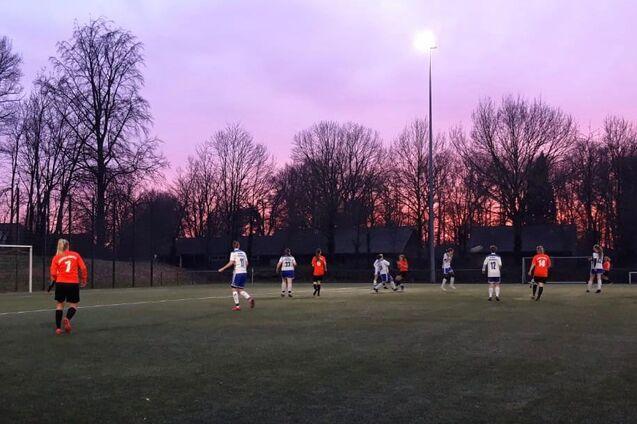 Fu&szlig;ballspiel auf einem Kunstrasenplatz bei D&auml;mmerung, Spieler in roten und wei&szlig;en Trikots auf dem Feld.