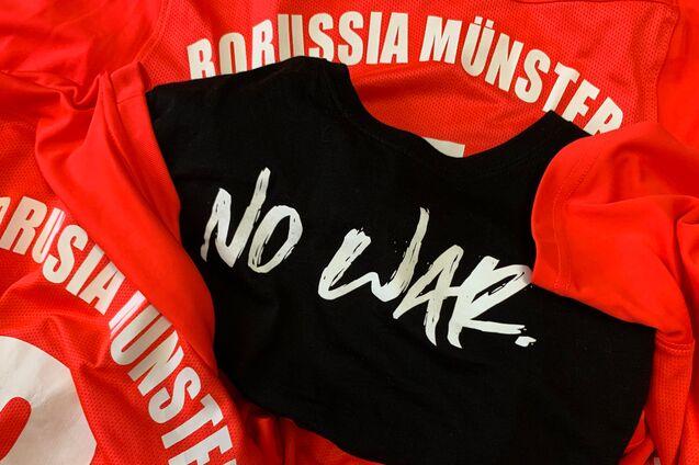 Rote Trikots mit der Aufschrift &bdquo;Borussia M&uuml;nster&ldquo; und einem schwarzen Shirt mit der Aufschrift &bdquo;NO WAR.&ldquo; in der Mitte.