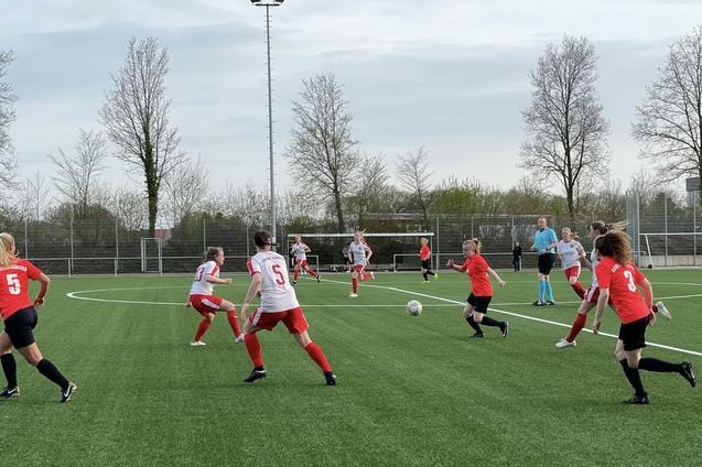 Fu&szlig;ballspiel zwischen zwei Teams auf einem Kunstrasenplatz; Spielerinnen in roten und wei&szlig;en Trikots laufen dem Ball nach.