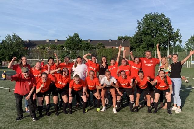 Gruppe von Frauen im roten Trikot jubelt auf einem Fu&szlig;ballplatz, einige halten Flaschen in der Hand.