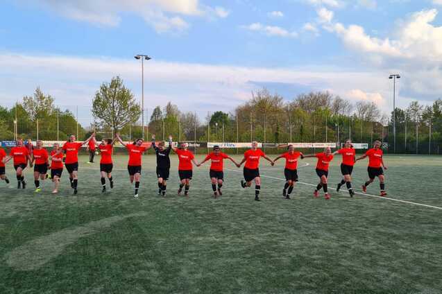 Eine Gruppe von Fu&szlig;ballspielerinnen in roten Trikots l&auml;uft Hand in Hand auf einem Kunstrasenfeld.