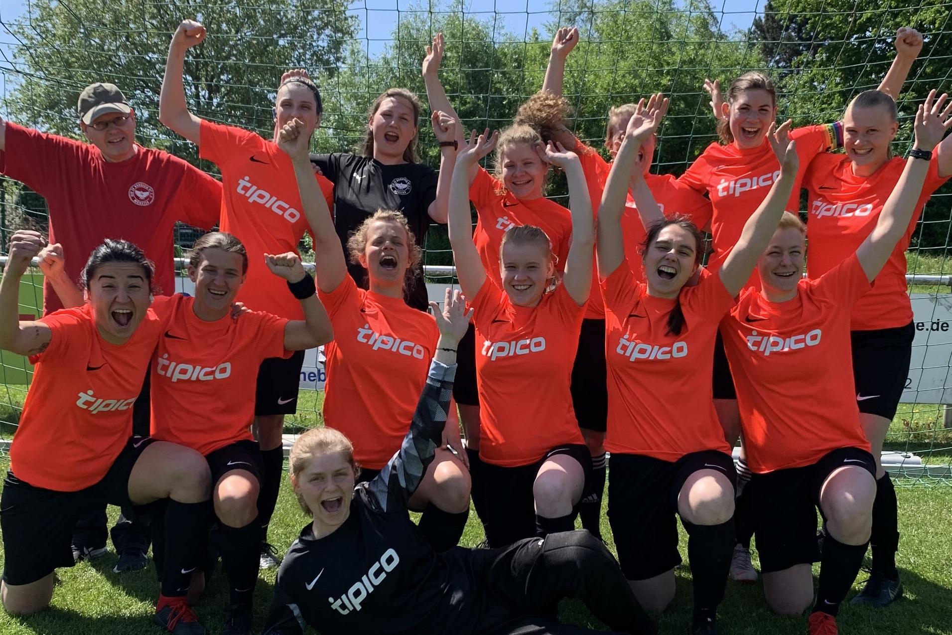 Gruppenfoto von 14 Fu&szlig;ballspielern in roten Trikots, die vor einem Tor auf einer Wiese jubeln und die Arme heben.