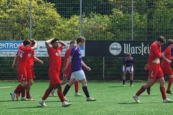 F&uuml;nf Fu&szlig;ballspieler in roten Trikots gehen auf einem Kunstrasenplatz, im Hintergrund ein Torwart in lila Trikot.