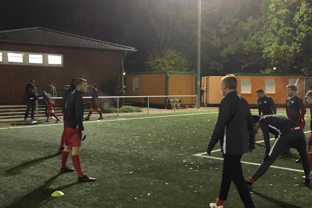 Fu&szlig;balltraining bei Nacht auf einem Kunstrasenplatz mit Spielern in rot-schwarzen Trikots und Konen.
