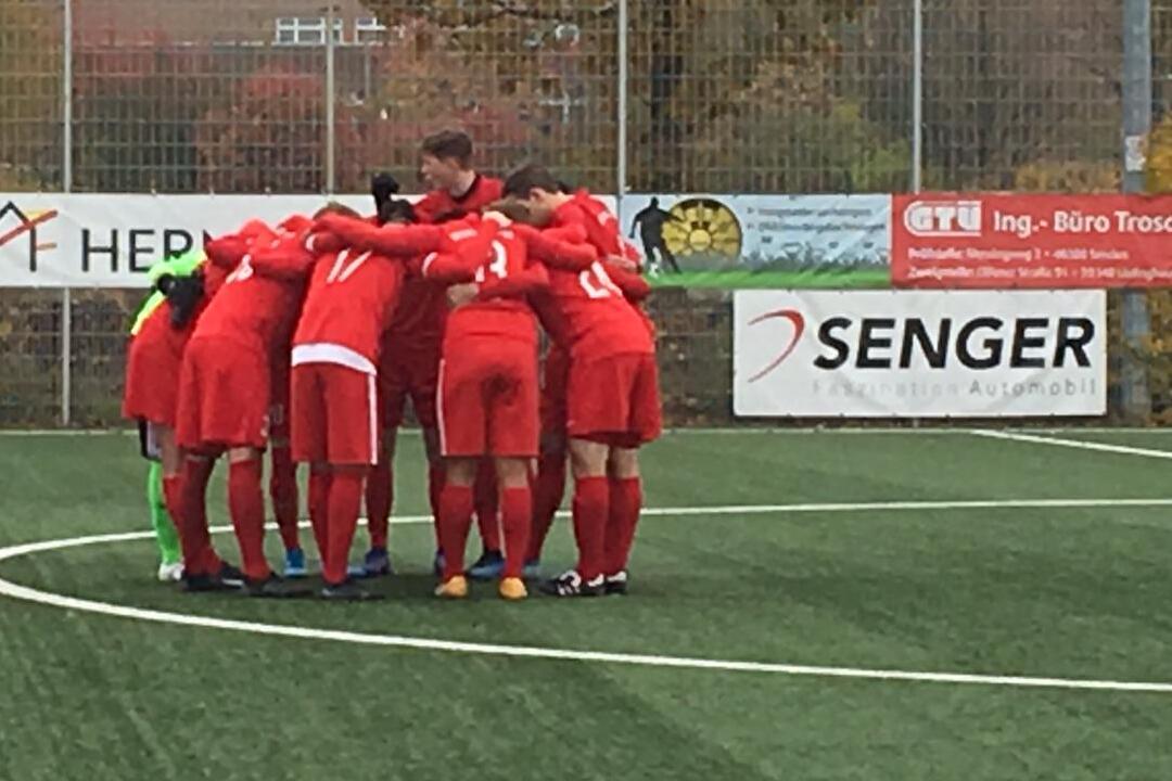 Fu&szlig;ballteam in roten Trikots bildet einen Kreis auf dem Platz und bereitet sich auf das Spiel vor.