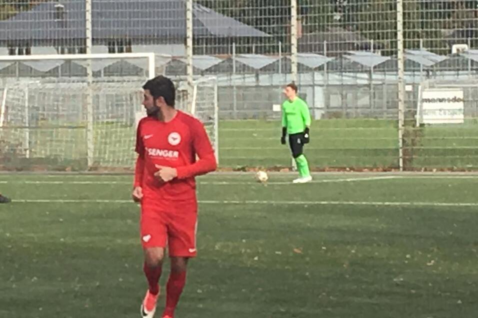 Spieler in roten Trikots auf einem Fu&szlig;ballfeld; im Hintergrund ein Torwart in gr&uuml;n vor dem Tor.