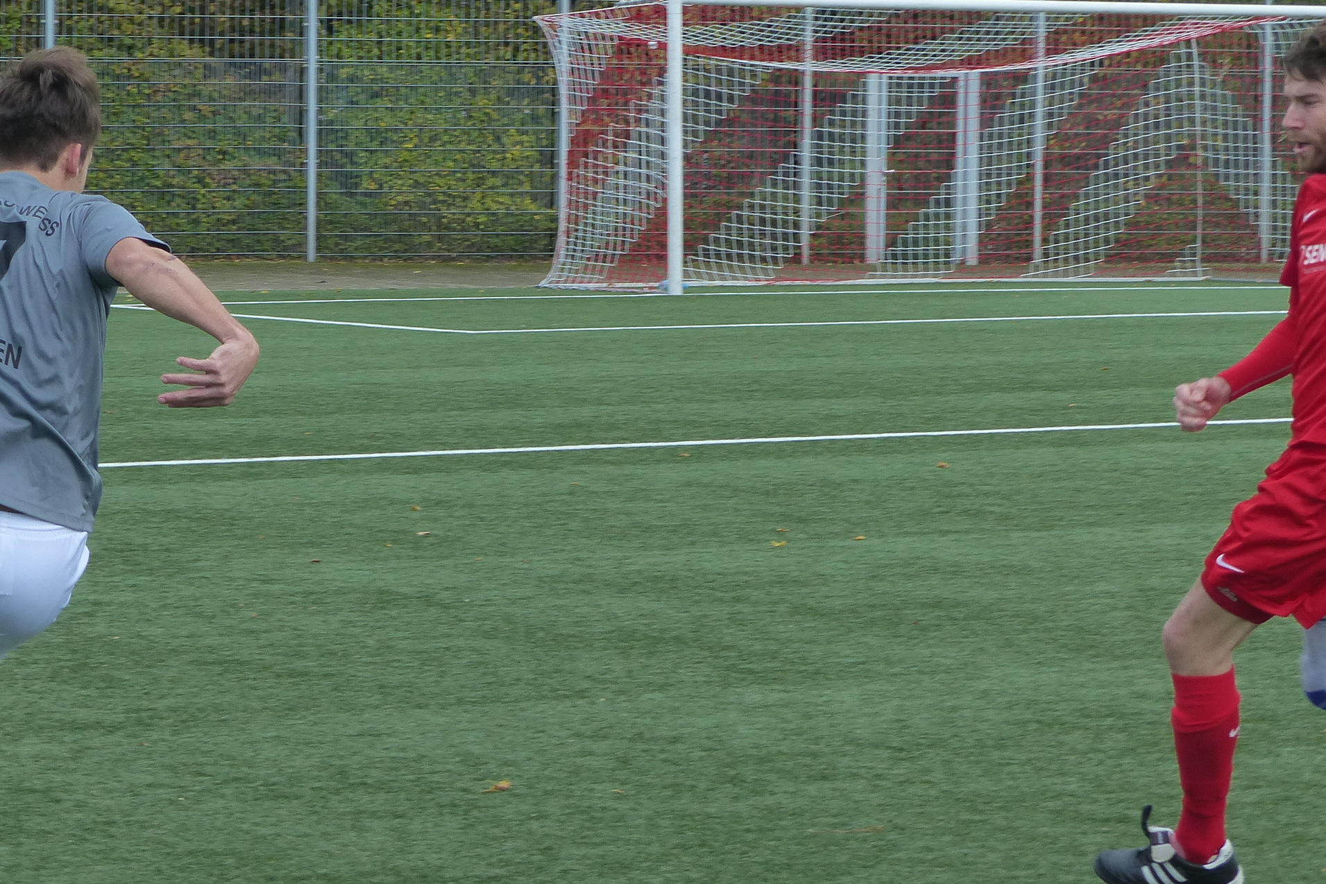 Zwei Fu&szlig;ballspieler in Aktion auf einem Kunstrasenplatz. Einer in grauem Trikot, der andere in rotem Trikot.