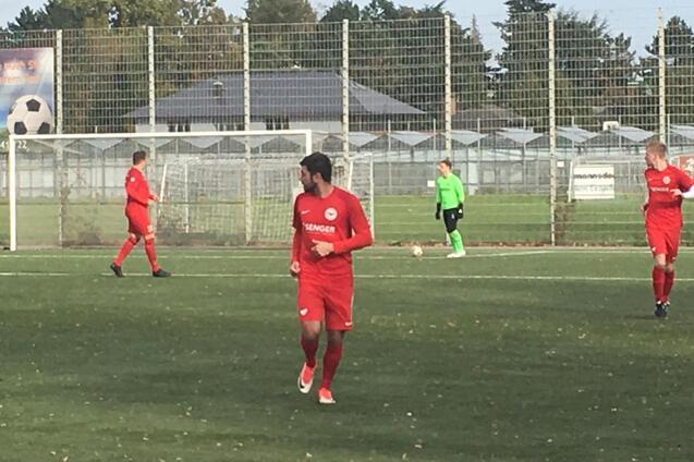 Spieler in roten Trikots auf einem Fu&szlig;ballfeld; im Hintergrund ein Torwart in gr&uuml;n vor dem Tor.