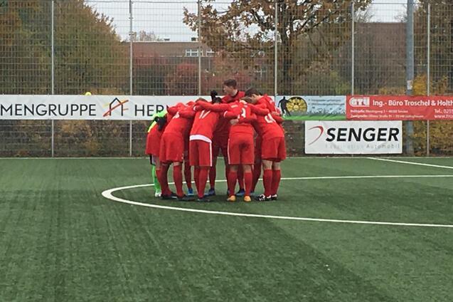 Fu&szlig;ballteam in roten Trikots bildet einen Kreis auf dem Platz und bereitet sich auf das Spiel vor.