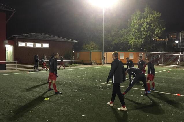 Fu&szlig;balltraining bei Nacht auf einem Kunstrasenplatz mit Spielern in rot-schwarzen Trikots und Konen.