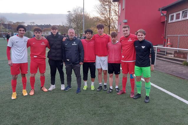 Gruppe von acht Fu&szlig;ballspielern in roten Trikots und einem Trainer auf einem Kunstrasenplatz.