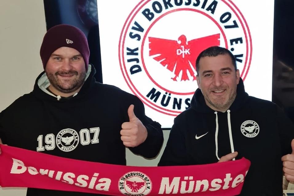 Zwei M&auml;nner zeigen Daumen hoch und halten einen Schal mit dem Schriftzug &bdquo;Borussia M&uuml;nster&ldquo; vor einem Vereinslogo.