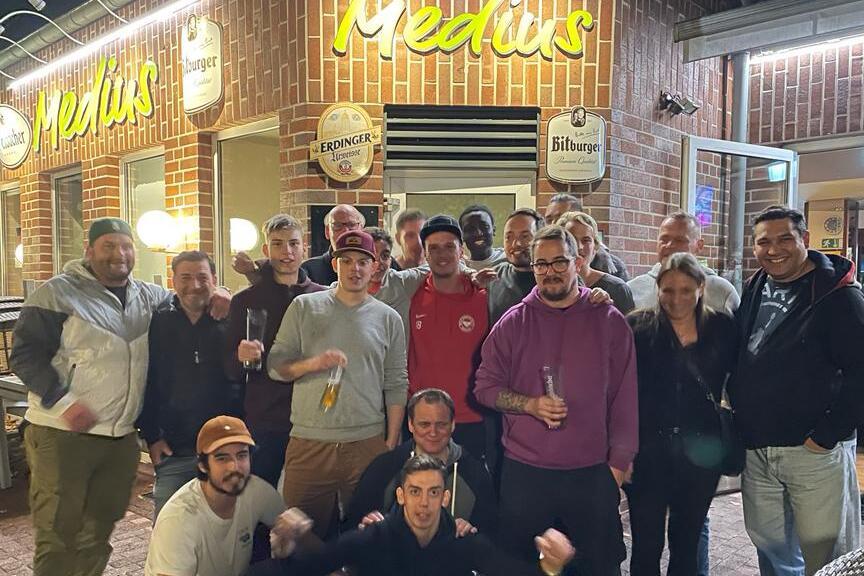 Gruppenshot von 18 Personen vor dem Restaurant "Medus", bei Nacht in urbaner Umgebung.