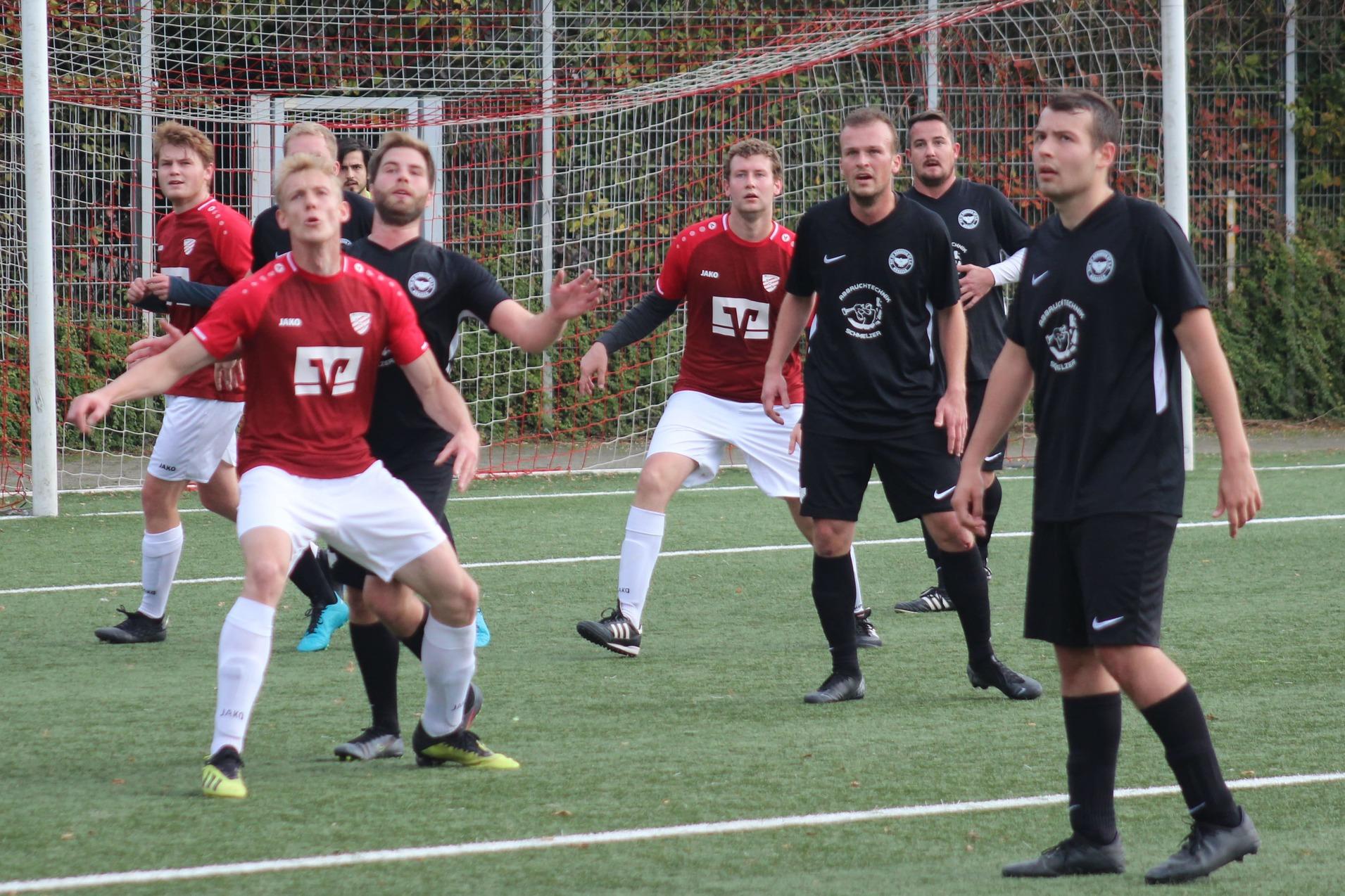 Zwei Fu&szlig;ballmannschaften in rot-wei&szlig;en und schwarzen Trikots stehen auf einem Kunstrasenplatz, w&auml;hrend sie auf den Ball achten.