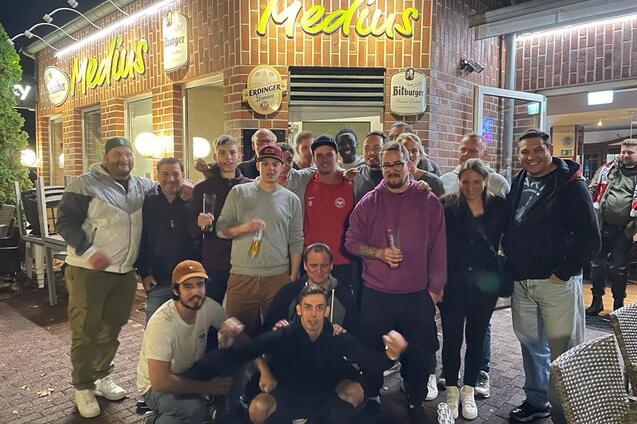 Gruppenshot von 18 Personen vor dem Restaurant "Medus", bei Nacht in urbaner Umgebung.