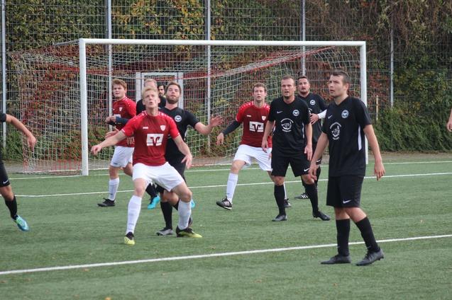 Zwei Fu&szlig;ballmannschaften in rot-wei&szlig;en und schwarzen Trikots stehen auf einem Kunstrasenplatz, w&auml;hrend sie auf den Ball achten.