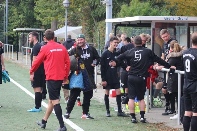 Spieler einer Fu&szlig;ballmannschaft stehen an der Bank, einige lachen und unterhalten sich, w&auml;hrend B&auml;lle im Hintergrund liegen.