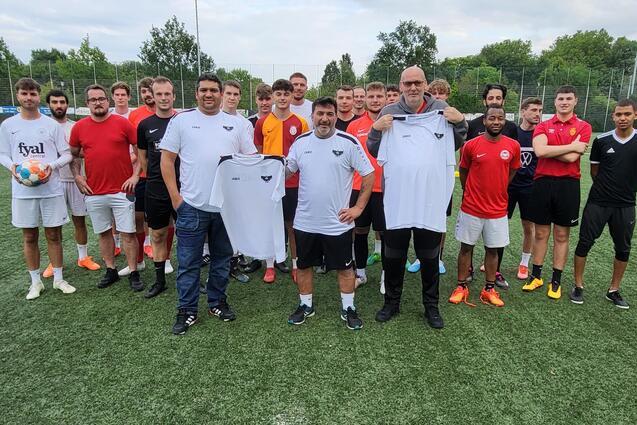 Gruppe von 22 Fu&szlig;ballspielern in Sportkleidung auf einem Kunstrasenplatz, einige halten Trikots in den H&auml;nden.