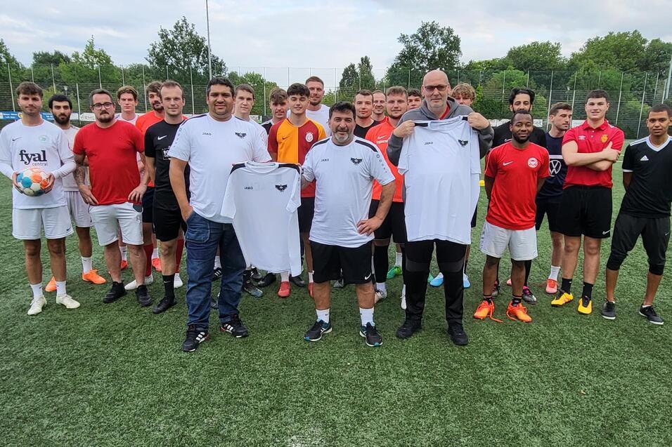 Gruppe von 22 Fu&szlig;ballspielern in Sportkleidung auf einem Kunstrasenplatz, einige halten Trikots in den H&auml;nden.
