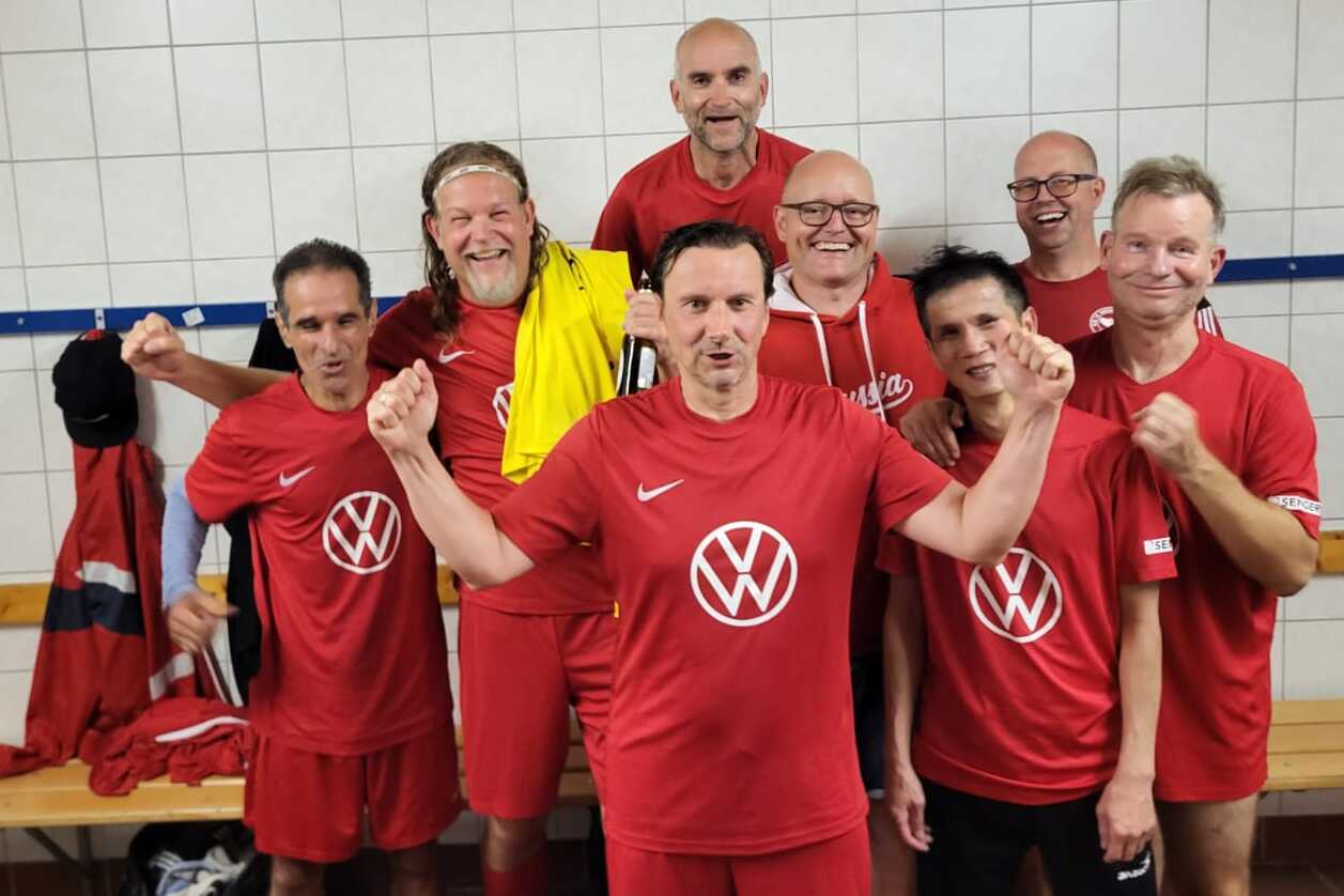 Gruppe von sportlichen M&auml;nnern in roten Trikots posiert in einer Umkleidekabine, l&auml;chelnd und motiviert.