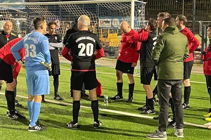 Gruppe von Fu&szlig;ballspielern und Schiedsrichtern in sportlicher Diskussion auf einem Kunstrasenplatz.