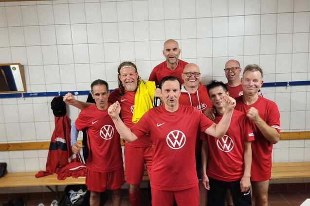 Gruppe von sportlichen M&auml;nnern in roten Trikots posiert in einer Umkleidekabine, l&auml;chelnd und motiviert.