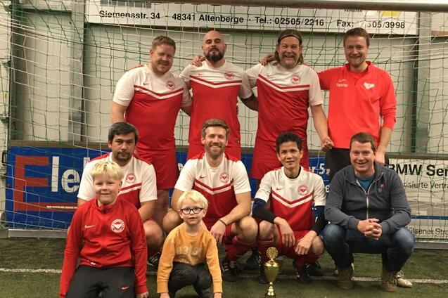 Gruppenfoto einer Fu&szlig;ballmannschaft mit Pokal, bestehend aus sechs Spielern und zwei Kindern im Vordergrund.
