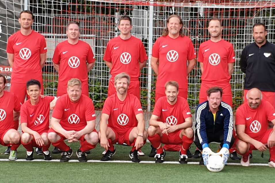 Mannschaftsfoto einer Fu&szlig;ballmannschaft in roten Trikots mit Volkswagen-Logo vor einem Tor auf einem Kunstrasenplatz.