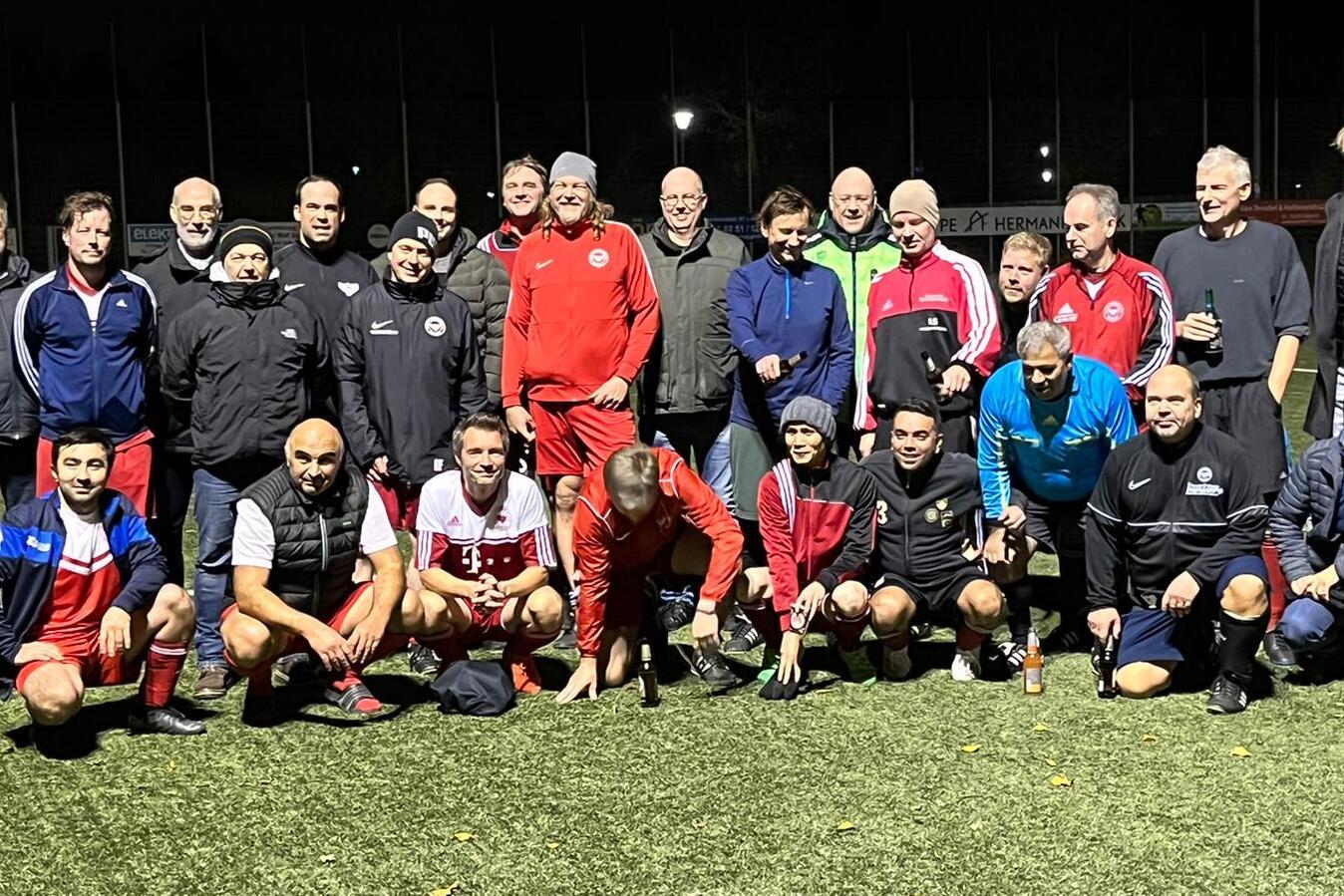 Gruppenfoto von Spielern und Trainern auf einem Fu&szlig;ballfeld bei Nacht, umringt von gr&uuml;ner Kunstrasenfl&auml;che.