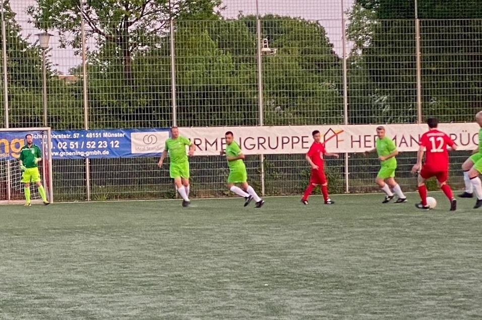 Zwei Fu&szlig;ballmannschaften in roten und gr&uuml;nen Trikots spielen auf einem Kunstrasenplatz.