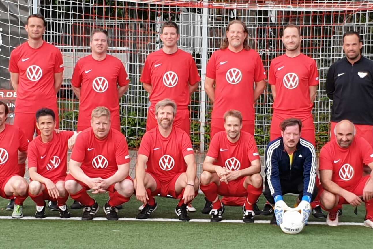 Mannschaftsfoto einer Fu&szlig;ballmannschaft in roten Trikots mit Volkswagen-Logo vor einem Tor auf einem Kunstrasenplatz.