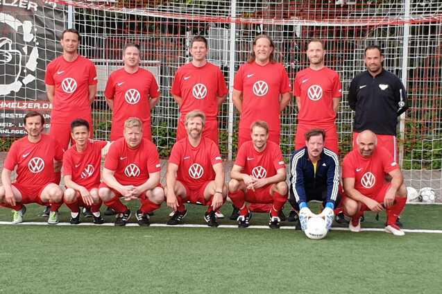 Mannschaftsfoto einer Fu&szlig;ballmannschaft in roten Trikots mit Volkswagen-Logo vor einem Tor auf einem Kunstrasenplatz.