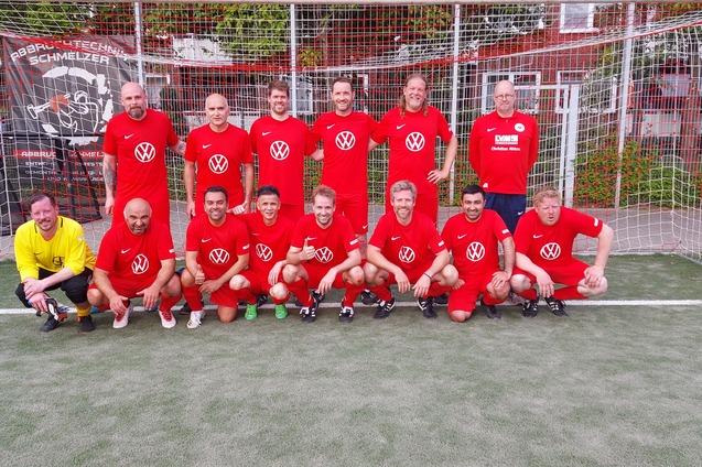 Gruppenfoto von elf Fu&szlig;ballspielern in roten Trikots vor einem Tor. Ein Torwart in Gelb sitzt vorne.