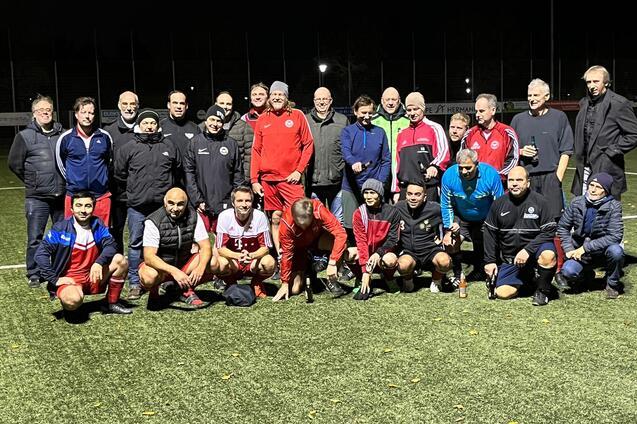 Gruppenfoto von Spielern und Trainern auf einem Fu&szlig;ballfeld bei Nacht, umringt von gr&uuml;ner Kunstrasenfl&auml;che.