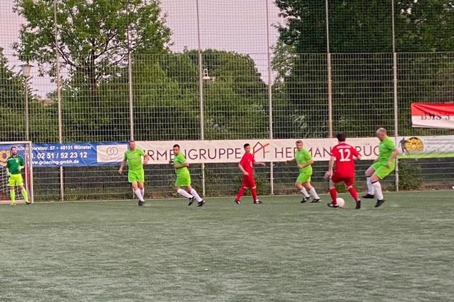 Zwei Fu&szlig;ballmannschaften in roten und gr&uuml;nen Trikots spielen auf einem Kunstrasenplatz.