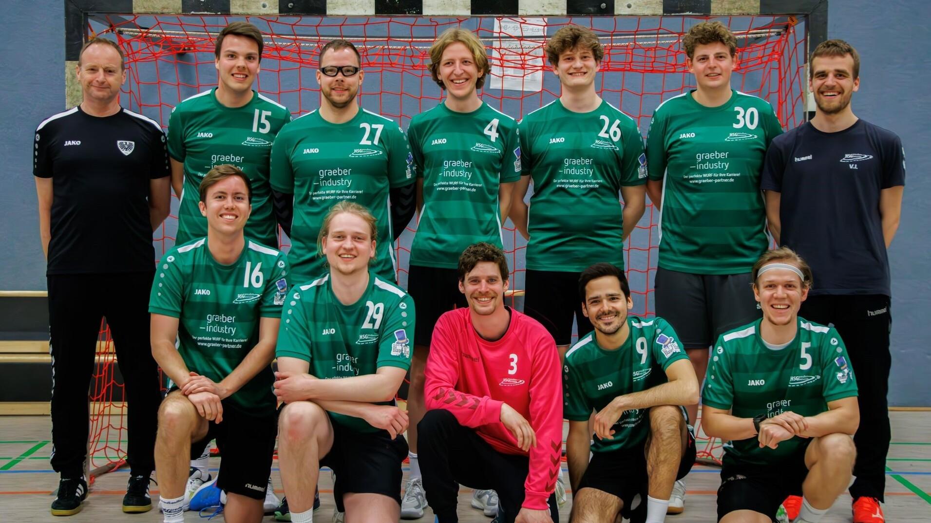 Mannschaftsfoto einer Handballmannschaft in gr&uuml;nen Trikots vor einem roten Tor.