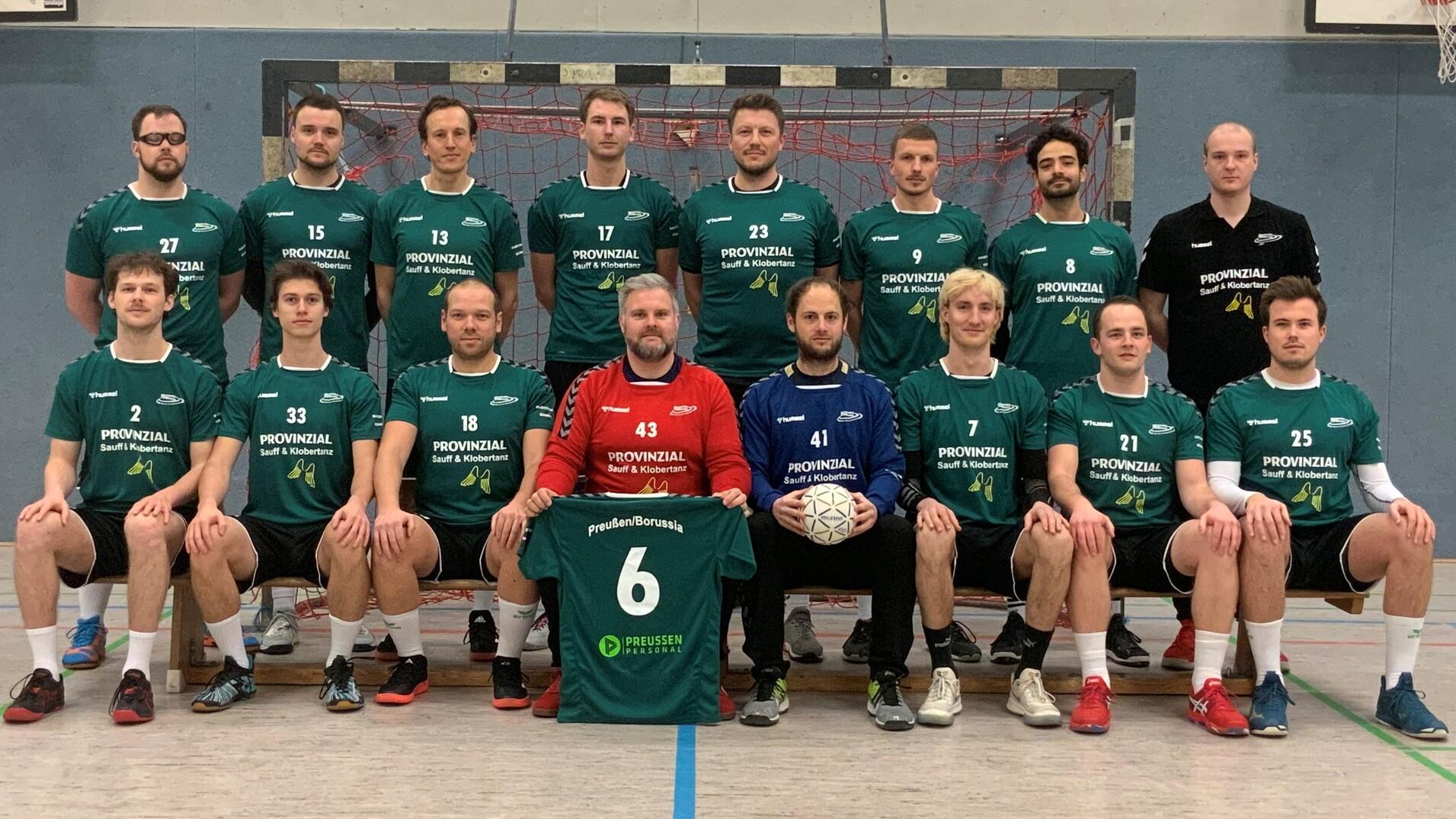 Mannschaftsfoto einer Handballmannschaft in gr&uuml;nen Trikots, aufgestellt vor einem Handballtor in einer Sporthalle.
