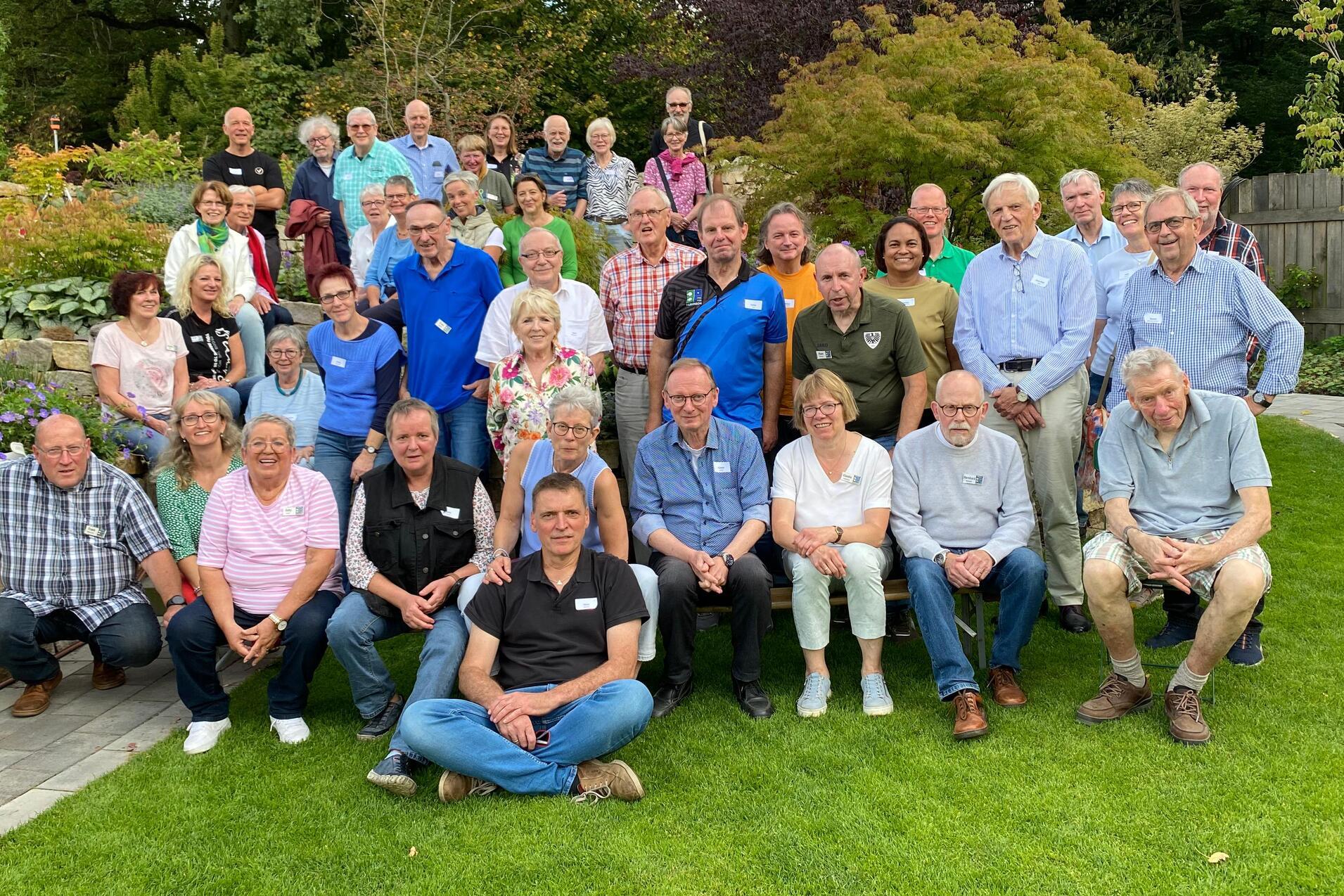 Gruppenfoto von etwa 40 Personen im Garten, umgeben von Pflanzen und B&auml;umen, l&auml;chelnd und in festlicher Stimmung.